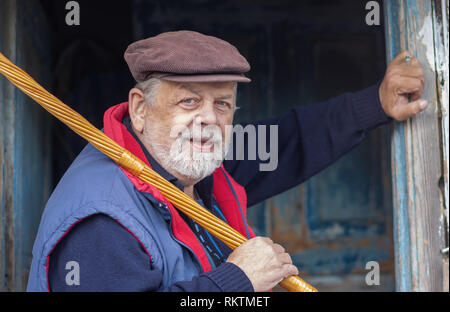 Schönes Portrait von ukrainischen Bärtigen älteren Bauern, gegen sein Haus Eintrag und halten Walking Stick auf der Schulter Stockfoto