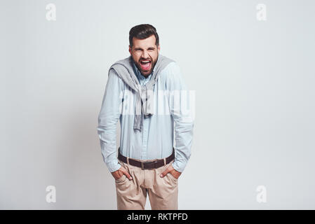Es ist Ihre Schuld. Zornigen jungen Mann schaut sich Kamera und Schreien, die Hände in den Taschen, während gegen grauen Hintergrund stehen. Negative Emotion Stockfoto