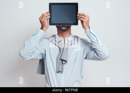 Android. Bärtiger Mann in Freizeitkleidung hält seine digitalen Tablet vor seinem Gesicht, während gegen grauen Hintergrund stehen. Digitale Konzept. Close-up Stockfoto