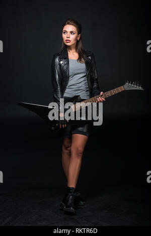 Schöne Frau in Leder Jacke mit E-Gitarre isoliert auf Schwarz Stockfoto
