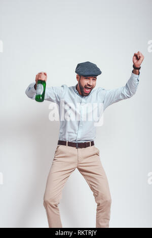 Partei auf. Betrunken brutalen Mann in hat mit einem Bier und Schreien während gegen grauen Hintergrund stehen. Close-up Portrait. Party Konzept. Stockfoto