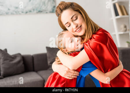 Kind und Mutter in rote Mäntel umarmen und zu Hause lächeln Stockfoto