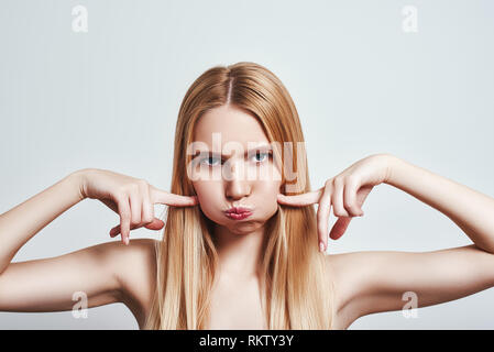 Studio shot von hartnäckigen junge blonde Frau, Blasen, Wangen und Gefühl verrückt. Menschliche Gefühle. CLose-up Stockfoto