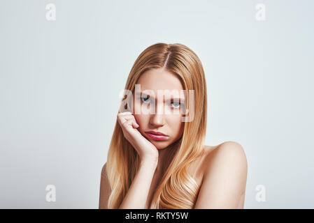 Gelangweilt. Junge blonde Frau an der Kamera schaut verärgert und ein trauriges Gesicht beim Stehen in der Studio auf einem grauen Hintergrund. Traurige Gefühle Stockfoto