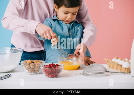 Cute little boy Schlagsahne Eier mit Ballon, während Mutter half ihm auf bicolor Hintergrund Stockfoto