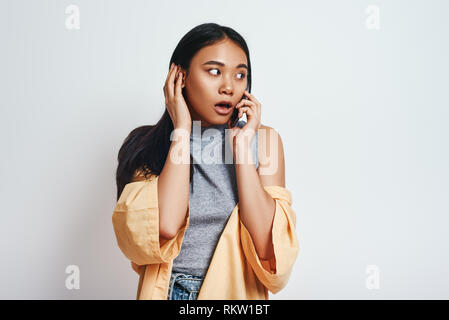 Oh mein Gott, Nahaufnahme, Porträt von überrascht asiatische Frau in Freizeitkleidung auf Ihr Smartphone beim Stehen in der Studio auf einem grauen Hintergrund. Menschliche Emotionen Stockfoto