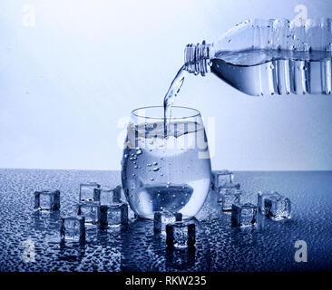 Pouring fresh drinking mineral water from plastic bottle. Glass filled with water over white background. Stockfoto