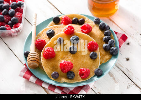 Pfannkuchen mit Himbeeren, Heidelbeeren und Honig auf weiße Holztisch. Stockfoto