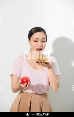 Junge schöne Mädchen mit Apfel und Kuchen in der Hand auf einem weißen Hintergrund. Gesunde Ernährung Konzept Stockfoto