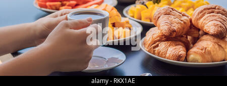 Eine junge Frau mit Frühstück auf dem Balkon. Frühstück mit Kaffee Obst und Brot, Croissant auf einem Balkon vor dem Hintergrund der großen Stockfoto