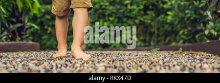 Junge gehen auf eine strukturierte, mit Kopfstein Pflaster, Reflexzonenmassage. Pebble Stones auf dem Bürgersteig für Fußreflexzonenmassage BANNER lange Format Stockfoto