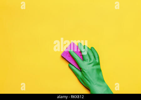 Eine Hand in einem Gummi- Handschuh mit einem rosa Schwamm auf gelbem Hintergrund. Reinigung Konzept. Stockfoto