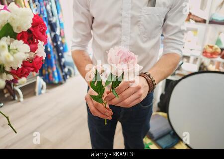 Der Typ im weißen Shirt rosa Pfingstrose in der Hand hält, auf den Blumen konzentrieren. Stockfoto