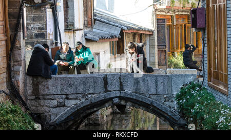 Die Menschen auf beiden Seiten einer kleinen Brücke sitzen in Lijiang Altstadt, Yunnan, China Stockfoto