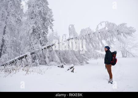 Jungen gutaussehenden Mann in Wanderausrüstung bewundern eine verschneite Wald während heraus für eine Wanderung im Winter Stockfoto