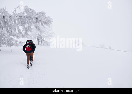 Rückspiegel eines jungen Paares in Wandern Gang zu Fuß durch Schnee bedeckt die Abwicklung durch einen Wald bei einer Winterwanderung Stockfoto