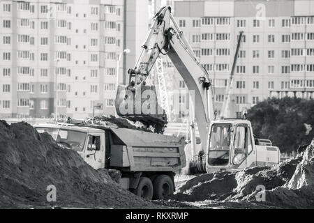 Bagger lädt die Erde in einen Dump Truck. Arbeiten auf der Baustelle. Stockfoto