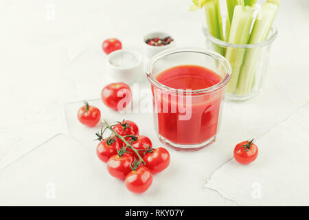 Glas leckeren Tomatensaft mit zwei gestreifte Trinkhalme, Stiele von frischen Sellerie, Salz, Pfeffer und frischen saftigen Kirschtomaten auf einem hellen Hintergrund. B Stockfoto