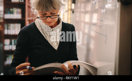 Nahaufnahme von einer älteren Frau, die in einer Bibliothek Blättern von Seiten eines Textes Buch. Ältere Frau Kontrolle für Bücher in der Universitätsbibliothek. Stockfoto