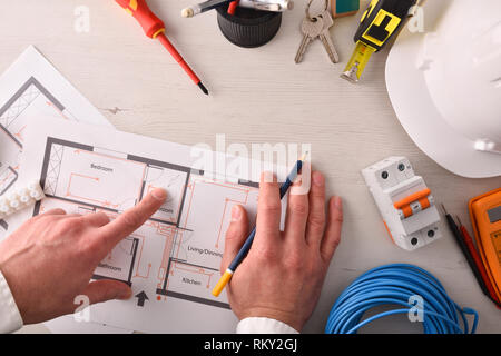 Techniker in der Elektrizität, die in einem elektrischen Schaltplan des Gehäuses Installation auf dem Schreibtisch mit Tools rund um. Horizontale Komposition. Top Stockfoto