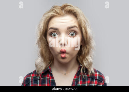 Portrait von Lustig begeistert schöne blonde junge Frau im casual rot kariertem Hemd stehen und von der Kamera mit großen Augen und Lippen. Stockfoto