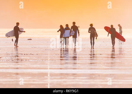 Eine Gruppe von Surfern, die ihre Surfbretter und von dort über den Fistral Beach am späten Abend die Sonne. Stockfoto