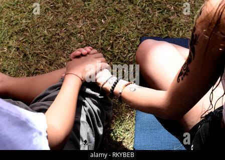 Zwei Frauen halten sich an den Händen sitzen im Schneidersitz auf dem Gras. Stockfoto