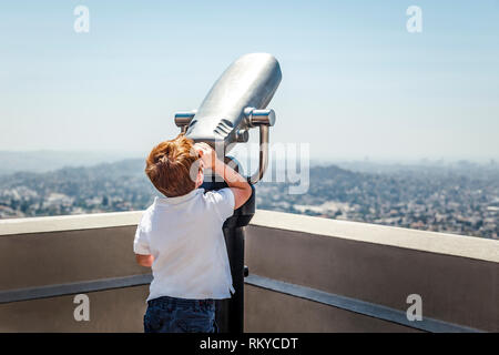 Junge rothaarige Junge schaut durch touristische Fernglas am Himmel in Los Angeles in Kalifornien. Stockfoto