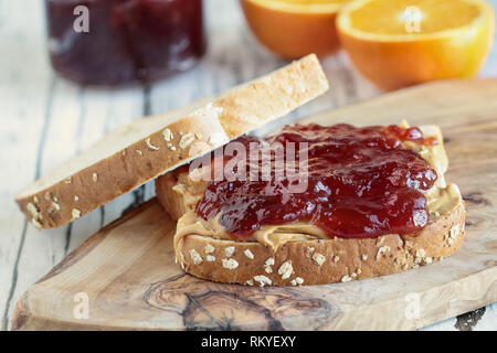 Hausgemachte Peanut Butter und Marmelade Sandwich auf Hafer Brot, über einen rustikalen Holzmöbeln Hintergrund mit Obst im Hintergrund bereit zum Mittagessen. Stockfoto