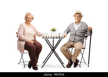 Volle Länge Portrait von einer alten Frau und älteren Mann sitzt an einem Tisch mit einer Tasse Kaffee und lächelnd in die Kamera isoliert auf weißem backgroun Stockfoto