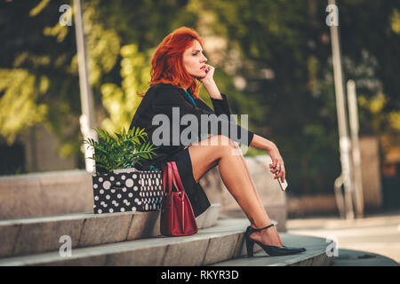 Ernste nachdenkliche business Frau sitzt auf der Treppe neben einer Kiste voller Ihr persönliches Eigentum von das Amt nur, nachdem Sie gefeuert. Stockfoto