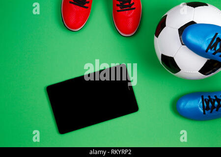 Fußball-Fußball-Hintergrund. Blick von oben auf die beiden Fußball-Spieler Schuhe, Fußball und Tablet Computer auf grünem Hintergrund Stockfoto