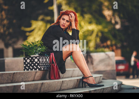 Ernste nachdenkliche business Frau sitzt auf der Treppe neben einer Kiste voller Ihr persönliches Eigentum von das Amt nur, nachdem Sie gefeuert. Stockfoto