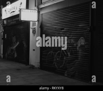 Rollläden aus Geschorenem Herrenfriseure und Bull's Bikes von Nacht, Edgware, London, UK. Stockfoto