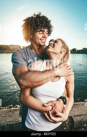 Schöne junge Paar ruht und umarmen Nach erfolgreicher Ausbildung durch den Fluss in den Sonnenuntergang. Stockfoto