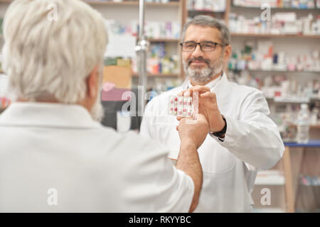 Happy Apotheker geben Kunden Blister mit Pillen für die Gesundheitsversorgung. Älterer mann Tabletten nehmen. Rentner Medikamente kaufen in der Apotheke. Konzept der pharmazeutischen Industrie. Stockfoto