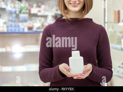 Nicht wiederzuerkennen, junge Frau, die in der Drogerie, posieren. Apotheke Kunden halten Weiße kosmetische Flasche in den Händen. Frau lächelnd. Konzept der Apotheke waren. Stockfoto