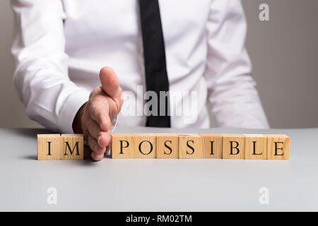 Holzklötze Rechtschreibung das Wort unmöglich mit Geschäftsmann wegdrücken Buchstaben im mit seiner Hand. Stockfoto