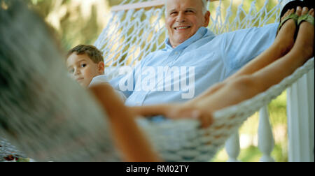 Portrait eines älteren Erwachsenen Mann in einer Hängematte sitzen mit seiner jungen Enkel während draußen. Stockfoto