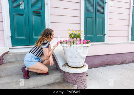 Junge hipster tausendjährigen Frau Gartenarbeit in New Orleans durch bunte Tür Architektur während der Tag mit rosa Blüten im Frühjahr und Sommer berühren Stockfoto