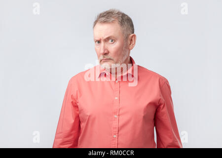 Älterer Mann im roten Hemd mit gerunzelter Stirn und schielen, Ungläubigkeit und Zweifel Stockfoto