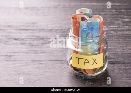 Glas Glas auf einem schwarzen Holztisch mit Münzen und Banknoten und den Worten steuern. Der Begriff des Rechts. Gericht und Entscheidung. Grundsteuer, Haus. Failur Stockfoto