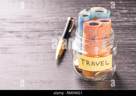 Glas Glas mit Münzen und Euro mit einem Stift und die Inschrift auf einem schwarzen Holztisch. Konzept der finanziellen Einsparungen für den großen Urlaub adventur Stockfoto