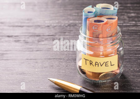 Glas Glas mit Münzen und Euro mit einem Stift und die Inschrift auf einem schwarzen Holztisch. Konzept der finanziellen Einsparungen für den großen Urlaub adventur Stockfoto