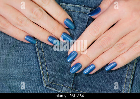 Detailansicht schöne weibliche Hände mit Blau glänzend professionelle Maniküre auf denim jeans Textur isoliert. Horizontale Farbfotografie. Stockfoto