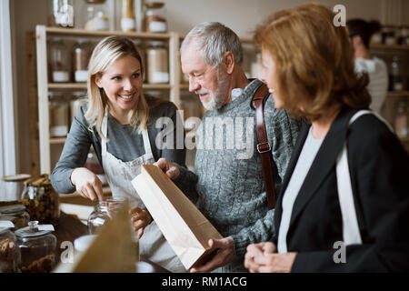 Eine weibliche Shop Assistant ein älteres Paar in einem Null steht für: - Abfall Shop. Stockfoto