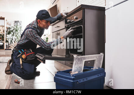 Nicht mit der Reparatur verzögern. Nahaufnahme der reparateur Backofen Prüfung mit einem Schraubendreher in der Küche im Koffer Stockfoto