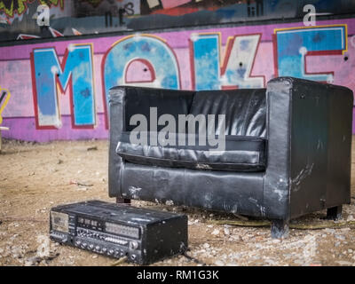 Schwarze Ledersessel und altes Radio in einem gekühlten kreative Schutz unter einer Brücke mit Graffitis im Hintergrund Stockfoto