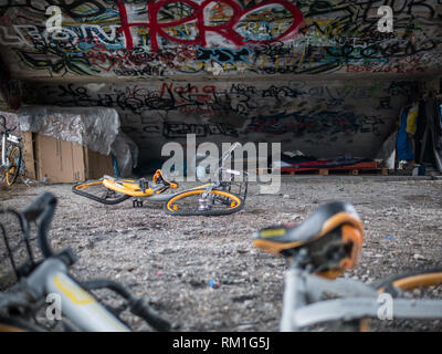 Alte gelbe Schrott, Fahrräder unter Beton Treppe mit Graffiti und Obdachlose schlafen Tierheim Stockfoto