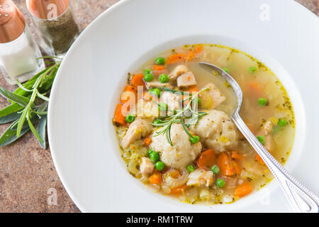 Selbstgemachte Hühnersuppe mit frischem Gemüse und hausgemachte Knödel serviert in einer weißen Schüssel mit Salz- und Pfefferstreuer und frischen Kräutern. Stockfoto